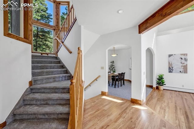 staircase featuring hardwood / wood-style flooring, a baseboard heating unit, and lofted ceiling with beams