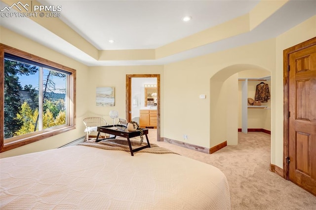 bedroom featuring connected bathroom, baseboard heating, light carpet, and a raised ceiling