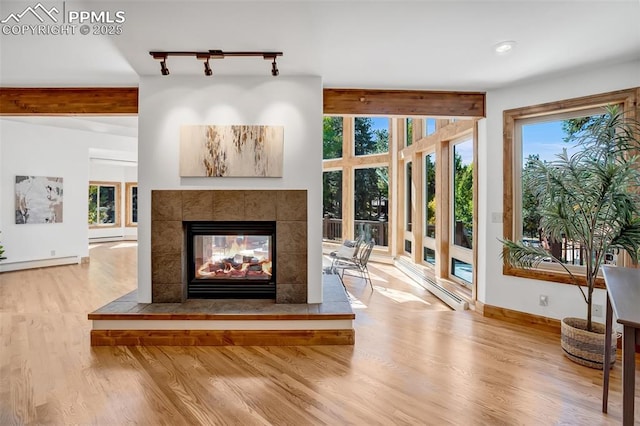 unfurnished living room with track lighting, wood-type flooring, a tiled fireplace, and baseboard heating