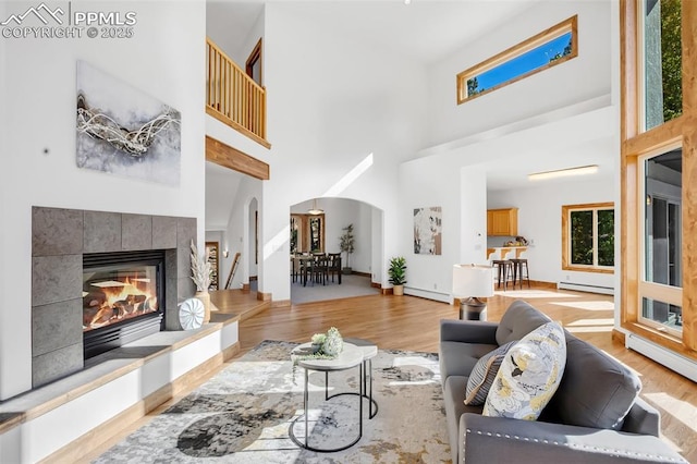 living room with a towering ceiling, a fireplace, light wood-type flooring, and a baseboard radiator