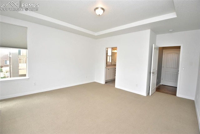 unfurnished bedroom with a raised ceiling, light carpet, and connected bathroom