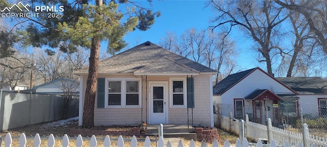 bungalow-style home with a fenced front yard and roof with shingles