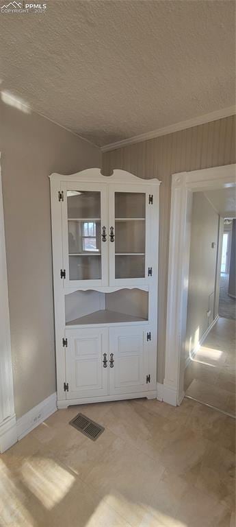 interior space with baseboards, a textured ceiling, visible vents, and crown molding