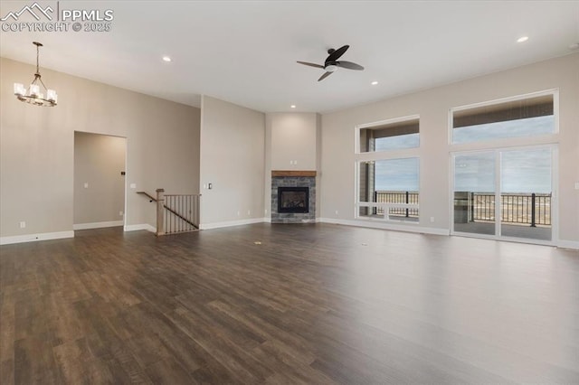 unfurnished living room featuring ceiling fan with notable chandelier, a fireplace, dark hardwood / wood-style floors, and a high ceiling