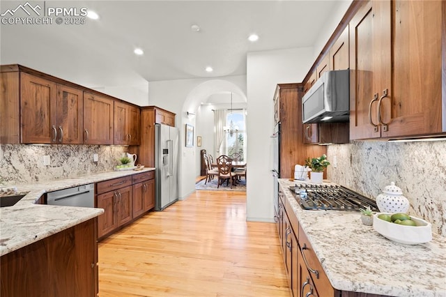 kitchen with stainless steel appliances, tasteful backsplash, decorative light fixtures, and light stone countertops