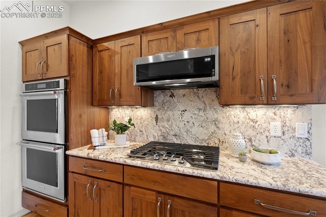 kitchen featuring appliances with stainless steel finishes, backsplash, and light stone countertops