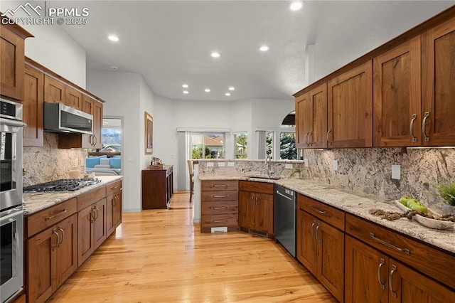 kitchen featuring appliances with stainless steel finishes, tasteful backsplash, light stone countertops, light hardwood / wood-style flooring, and sink