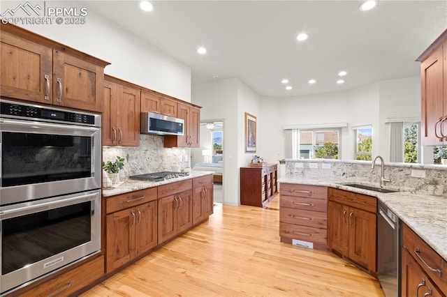 kitchen featuring decorative backsplash, sink, light hardwood / wood-style flooring, appliances with stainless steel finishes, and light stone counters