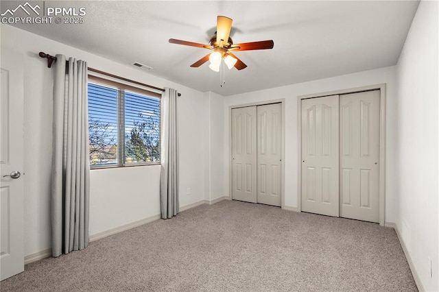 unfurnished bedroom featuring ceiling fan, light colored carpet, and multiple closets