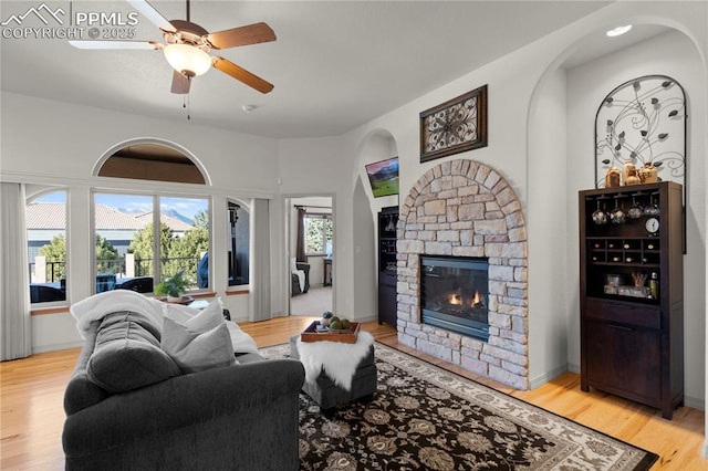 living room featuring ceiling fan, a wealth of natural light, light hardwood / wood-style flooring, and a fireplace