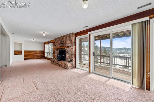 unfurnished living room featuring a textured ceiling, carpet floors, a mountain view, a wood stove, and wood walls