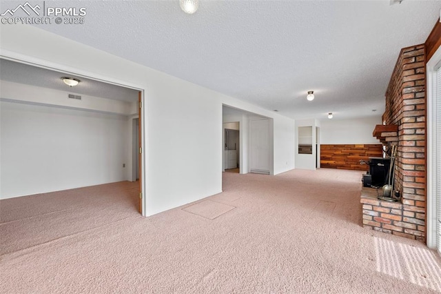 unfurnished living room with light carpet, wooden walls, and a textured ceiling