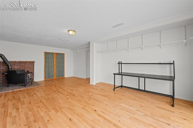 basement featuring light wood-type flooring, a wood stove, and a textured ceiling