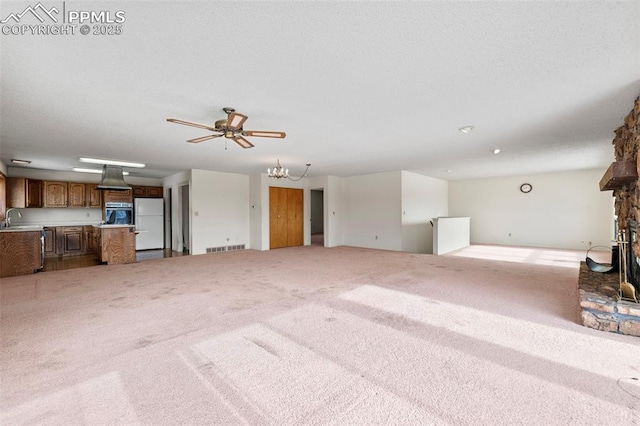 unfurnished living room with sink, ceiling fan with notable chandelier, a fireplace, and light carpet