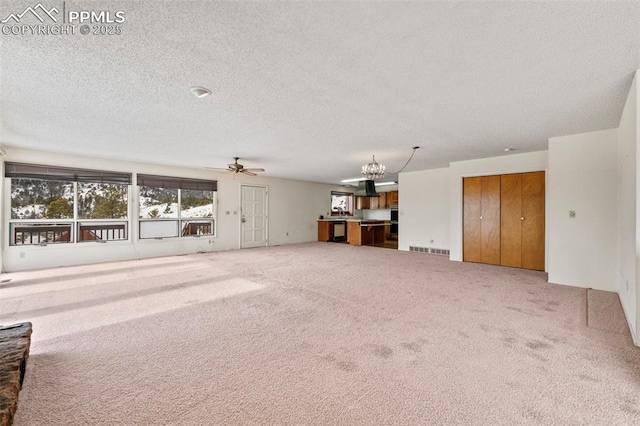 unfurnished living room with ceiling fan with notable chandelier, carpet, and a textured ceiling