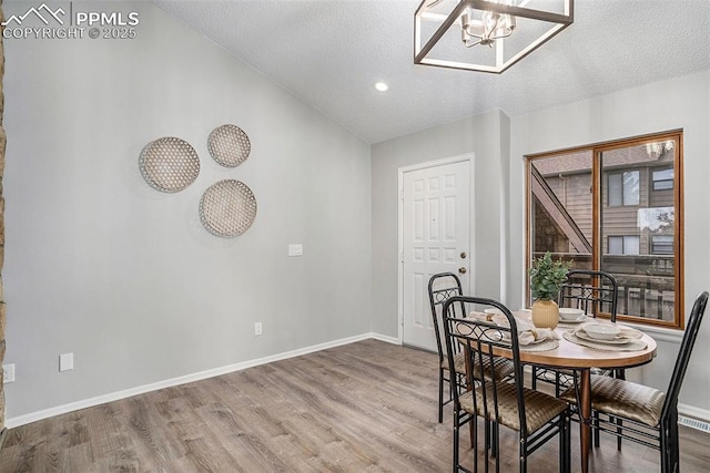 dining room with hardwood / wood-style flooring, a textured ceiling, vaulted ceiling, and a notable chandelier