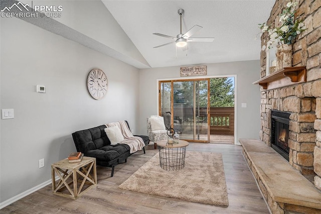 living room with ceiling fan, hardwood / wood-style floors, lofted ceiling, and a stone fireplace