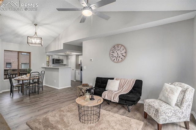 living room with wood-type flooring, ceiling fan with notable chandelier, a textured ceiling, and lofted ceiling