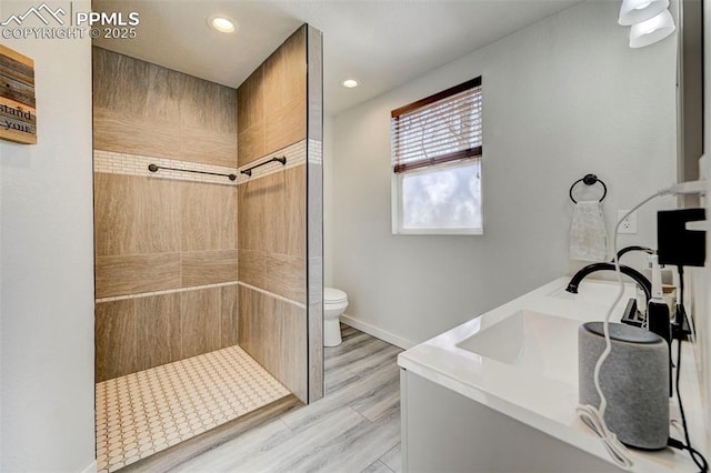 bathroom featuring wood-type flooring, toilet, tiled shower, and vanity