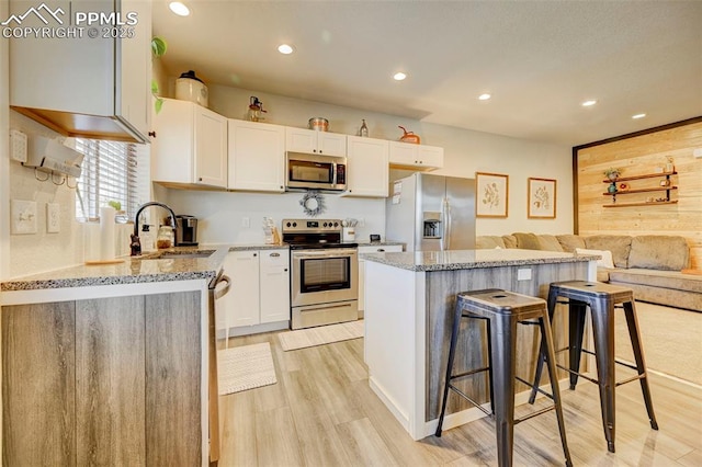 kitchen featuring appliances with stainless steel finishes, a kitchen breakfast bar, a kitchen island, white cabinets, and sink