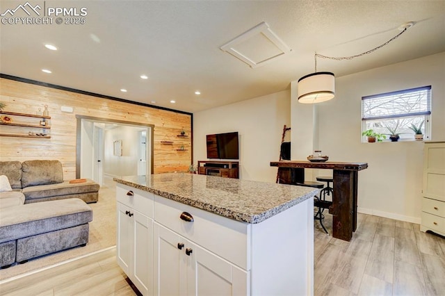 kitchen featuring wood walls, a kitchen island, white cabinetry, hanging light fixtures, and light stone countertops