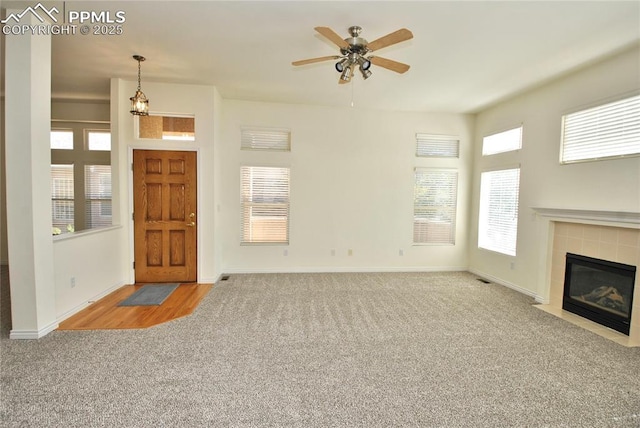 unfurnished living room with ceiling fan, light colored carpet, and a tile fireplace