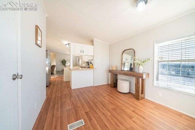 kitchen with white cabinets, stainless steel fridge, ornamental molding, and light hardwood / wood-style flooring