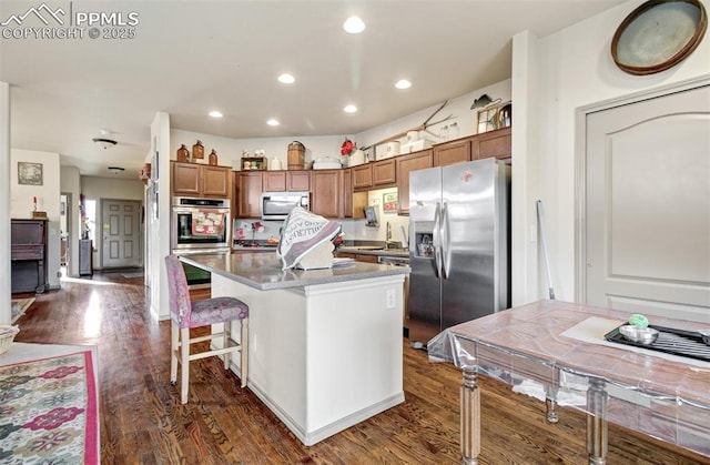 kitchen featuring a kitchen breakfast bar, appliances with stainless steel finishes, dark wood-type flooring, a kitchen island, and sink