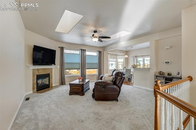 carpeted living room featuring a skylight, ceiling fan, and a tile fireplace