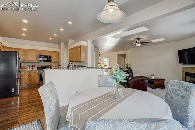 dining area with ceiling fan, sink, a tiled fireplace, hardwood / wood-style floors, and a skylight