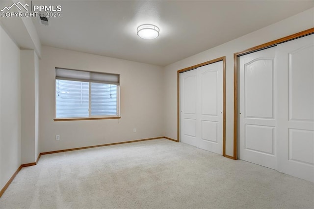 unfurnished bedroom featuring multiple closets and light colored carpet