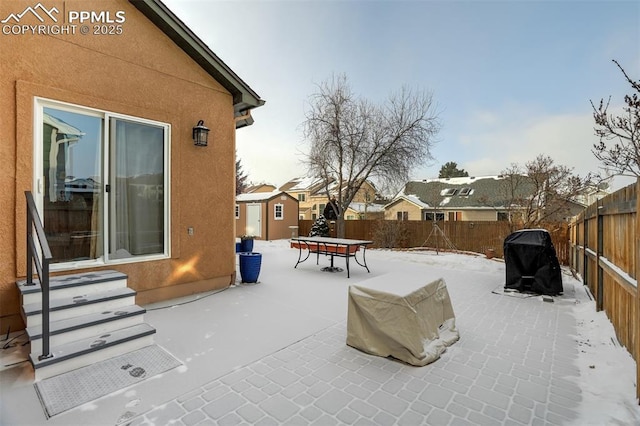 snow covered patio featuring grilling area and a storage shed