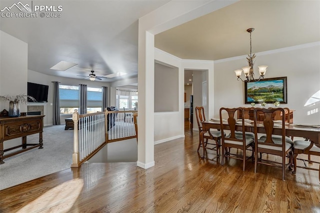 dining area with wood-type flooring, a tiled fireplace, ceiling fan with notable chandelier, and crown molding