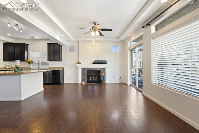 unfurnished living room with ceiling fan, a tray ceiling, dark hardwood / wood-style flooring, a tile fireplace, and sink