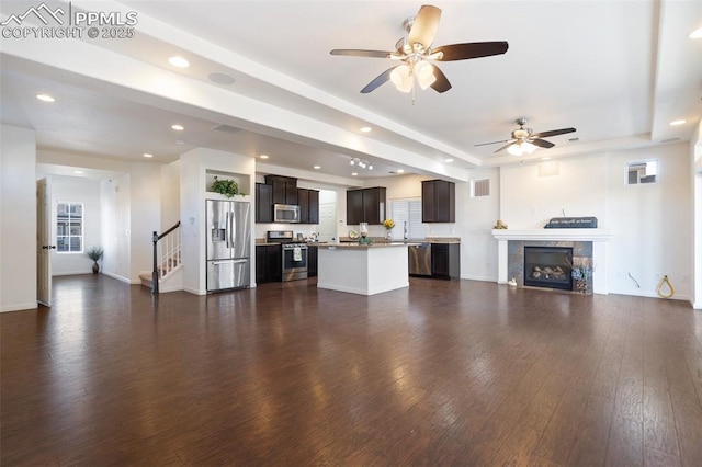 unfurnished living room featuring dark hardwood / wood-style floors, ceiling fan, a tiled fireplace, and a tray ceiling