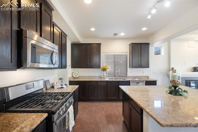 kitchen with appliances with stainless steel finishes, dark hardwood / wood-style floors, light stone counters, and sink