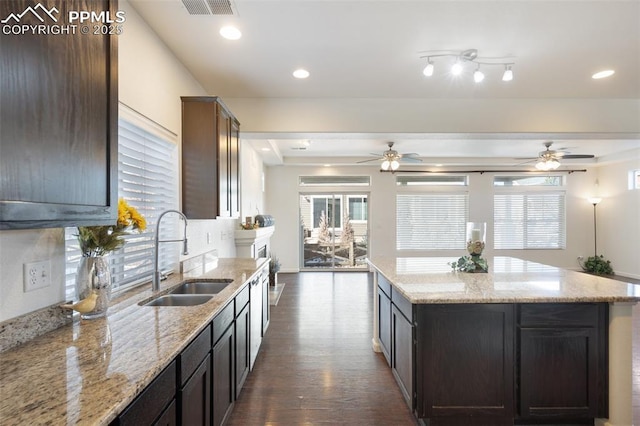 kitchen with a kitchen island, sink, dark wood-type flooring, dark brown cabinets, and light stone counters