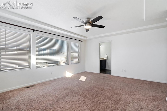 unfurnished bedroom with ceiling fan, ensuite bathroom, a tray ceiling, and carpet flooring