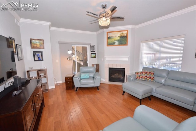 living room with ornamental molding, ceiling fan, light hardwood / wood-style floors, and a tiled fireplace