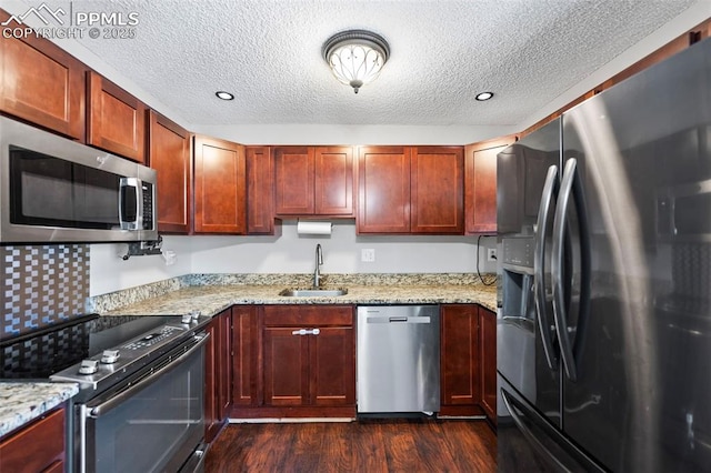 kitchen featuring dark wood-type flooring, a textured ceiling, light stone countertops, appliances with stainless steel finishes, and sink