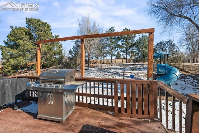 snow covered deck featuring a playground and area for grilling