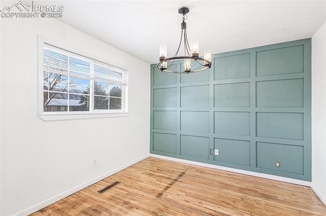 unfurnished dining area with a notable chandelier and light wood-type flooring