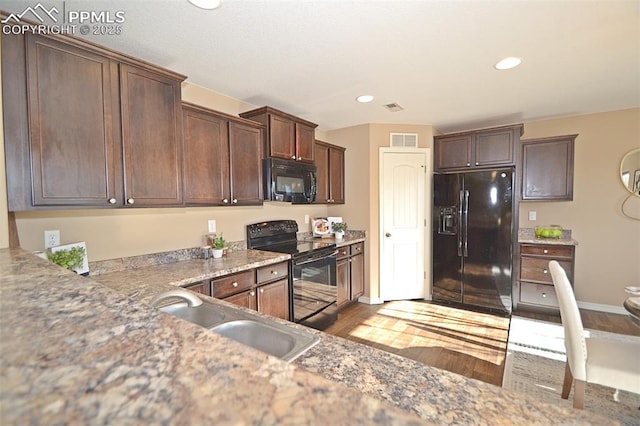 kitchen with sink, dark brown cabinets, light stone counters, black appliances, and light hardwood / wood-style floors