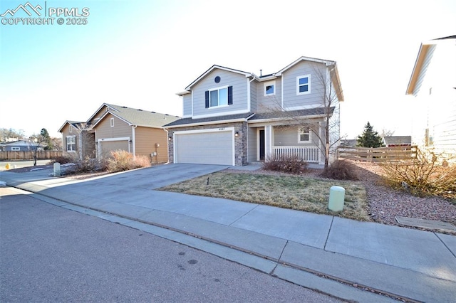 traditional home featuring a porch, concrete driveway, an attached garage, fence, and stone siding