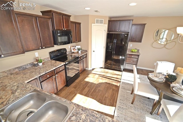 kitchen with sink, dark brown cabinetry, black appliances, light stone countertops, and light wood-type flooring