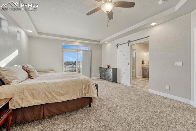 carpeted bedroom with access to outside, ceiling fan, a tray ceiling, a barn door, and ensuite bath