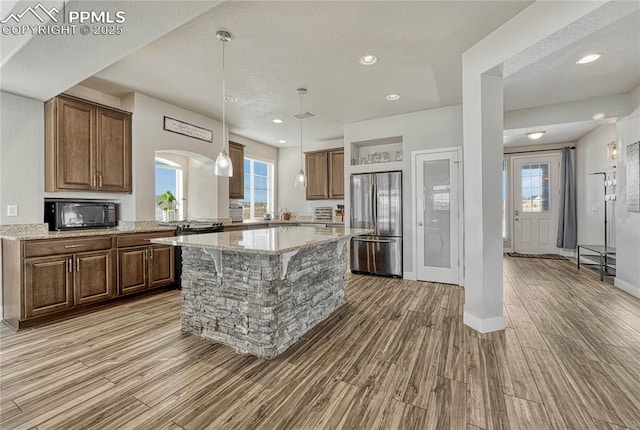 kitchen with a center island, pendant lighting, light stone counters, and stainless steel refrigerator