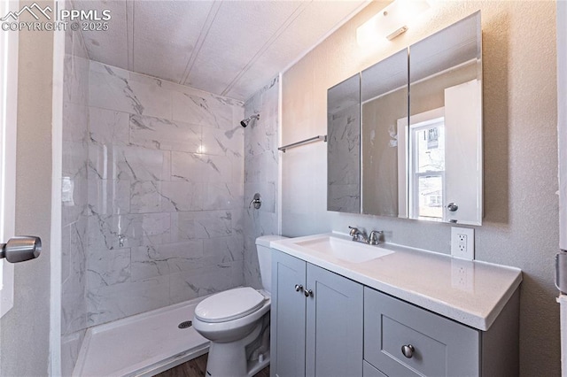 bathroom with a textured ceiling, a tile shower, vanity, and toilet