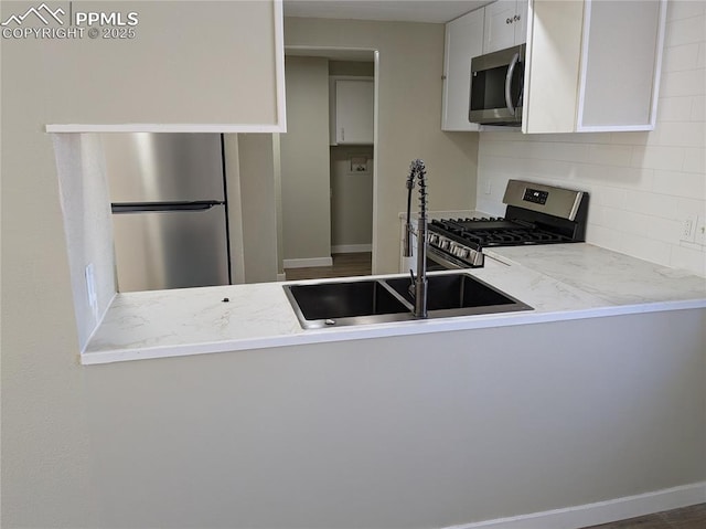 kitchen featuring light stone countertops, stainless steel appliances, tasteful backsplash, white cabinetry, and sink