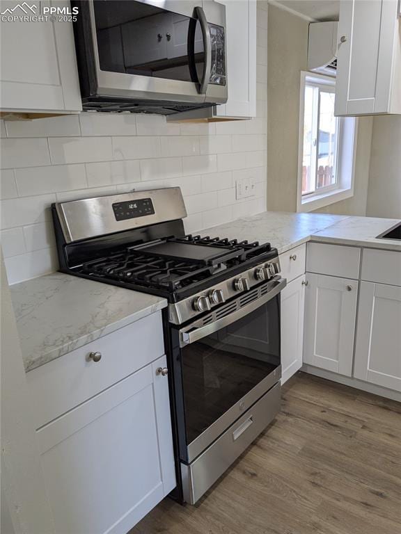 kitchen with light stone countertops, tasteful backsplash, light wood-type flooring, white cabinetry, and appliances with stainless steel finishes